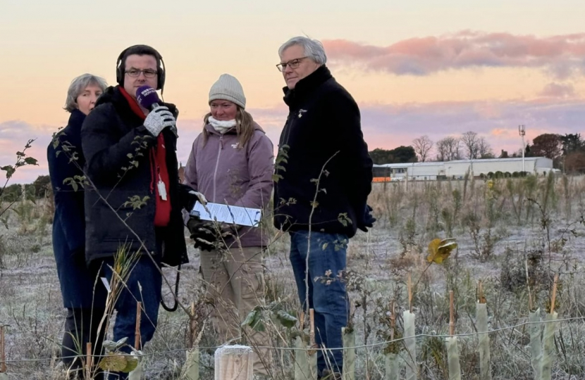 image shows news reporter with headphones and a microphone interviewing a group of people in a field covered with frost 